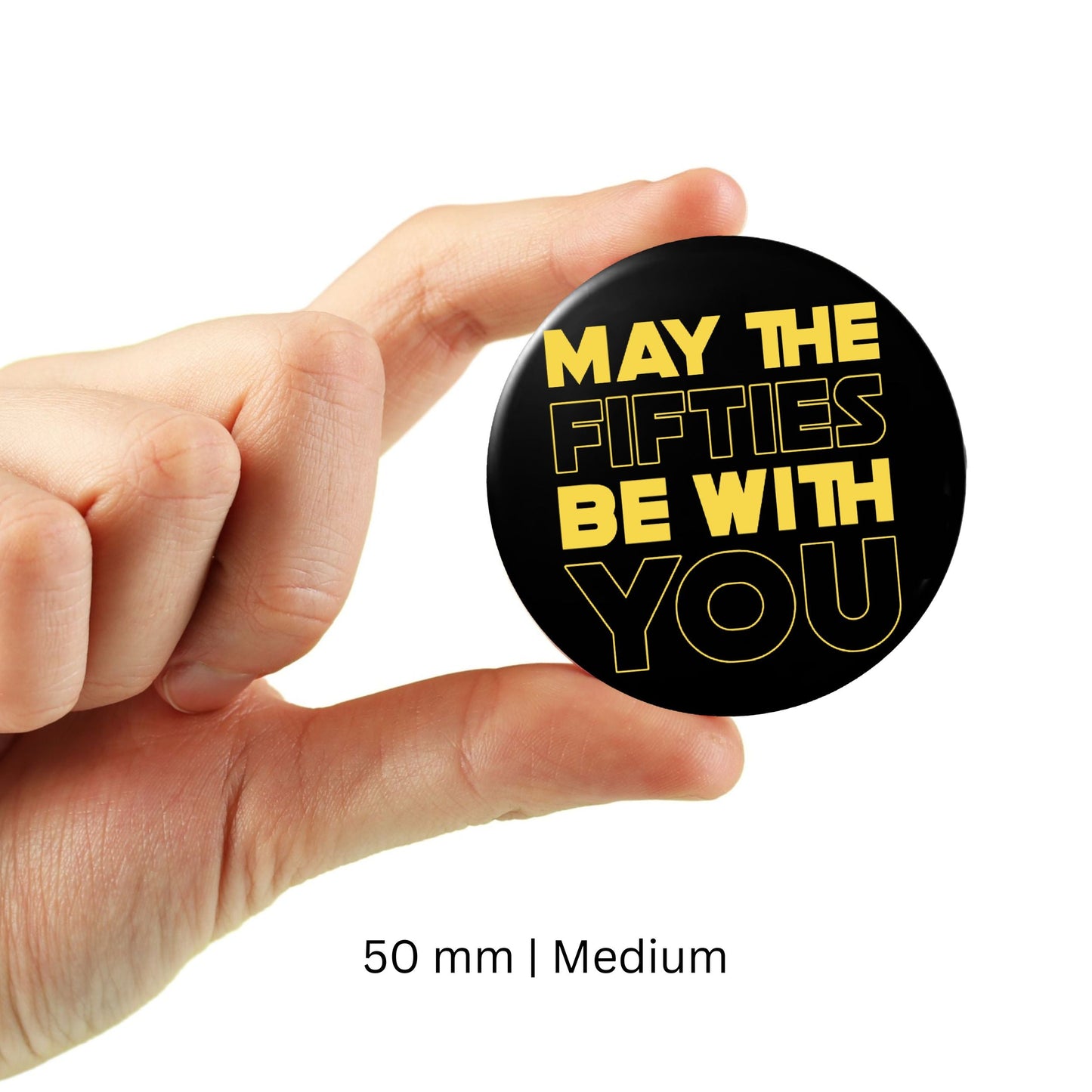 Person holding a "May The Fifties Be With You" black birthday badge, perfect for 50th birthday parties, size 50mm, medium.