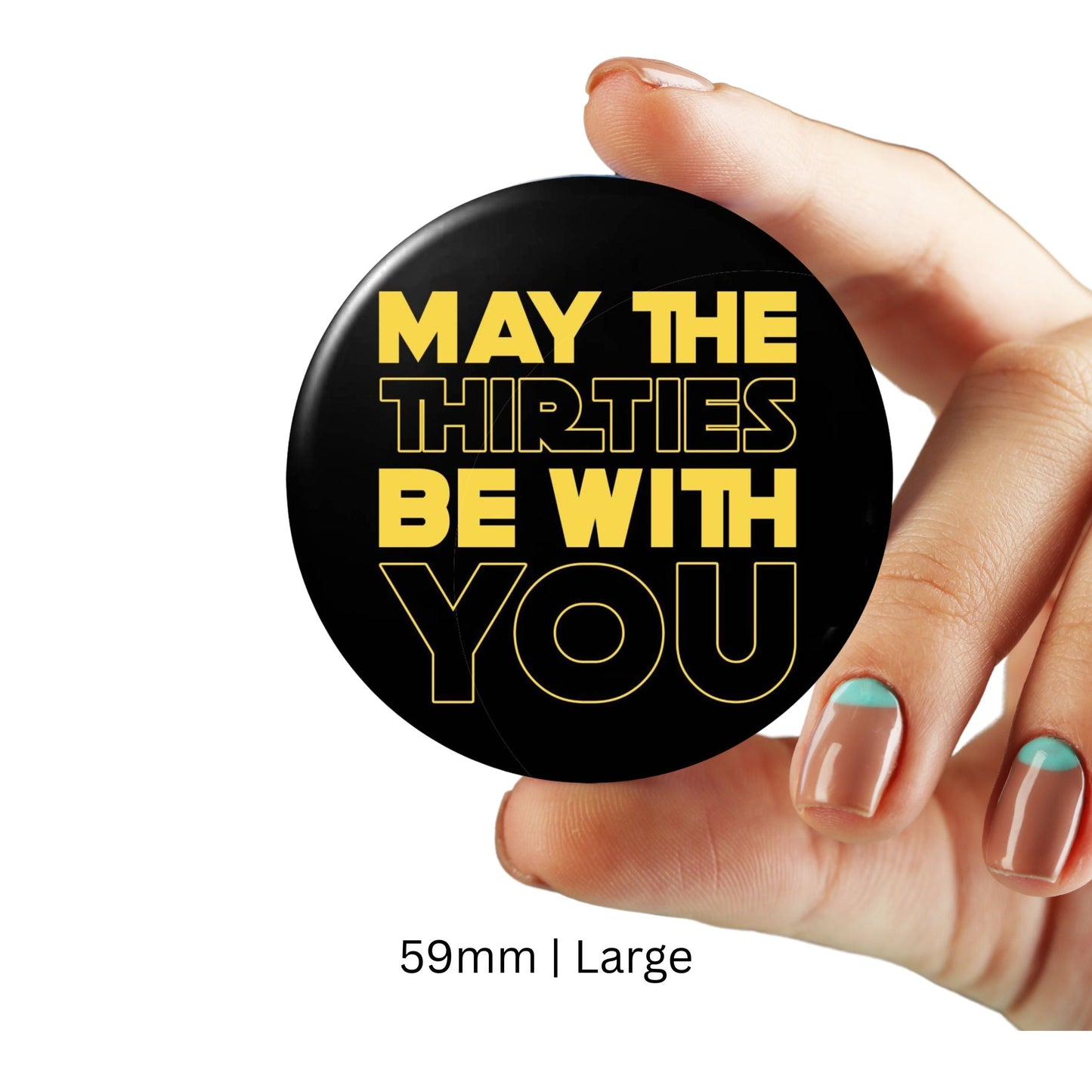 Hand holding a 59mm large black badge with yellow text 'May The Thirties Be With You', 30th birthday party accessory.
