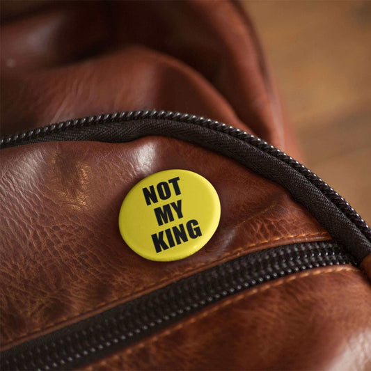 "Not My King" anti-monarchy pin badge on brown leather bag with zipper, 1 inch size, yellow color.