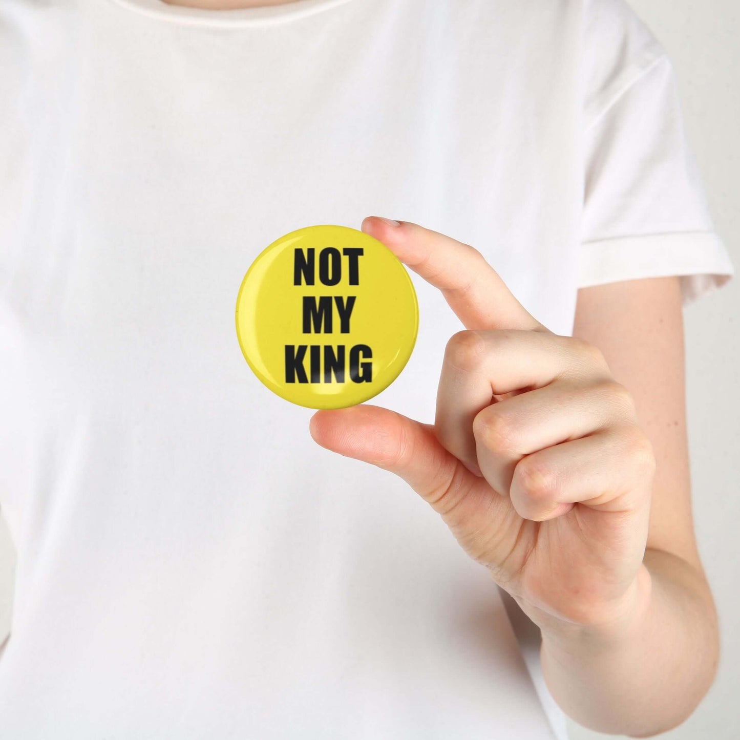 Person holding a yellow 'Not My King' anti-monarchy political pin button badge, highlighting minimalist activism design.