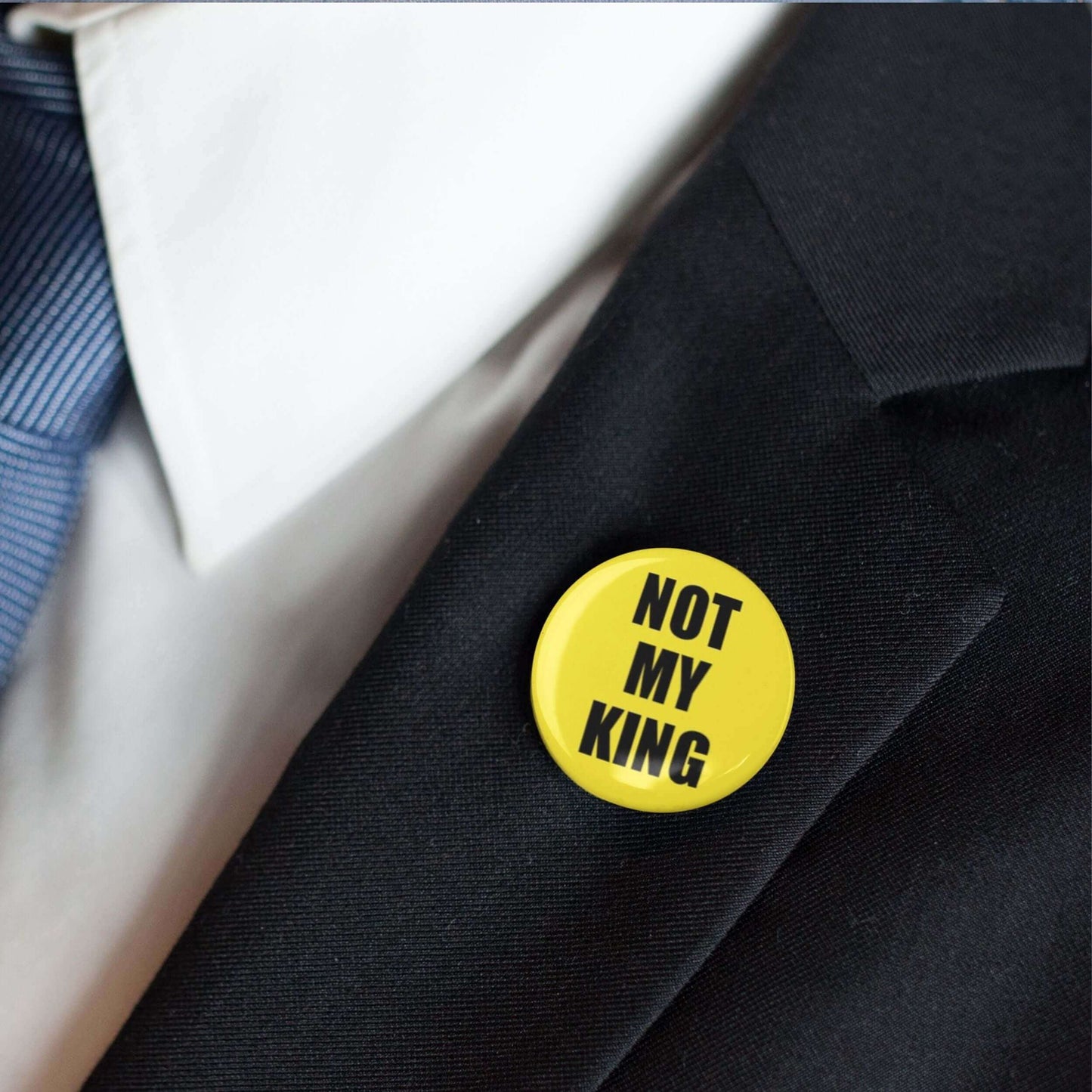 Person wearing Not My King anti-monarchy pin badge on black suit lapel, expressing political stance.