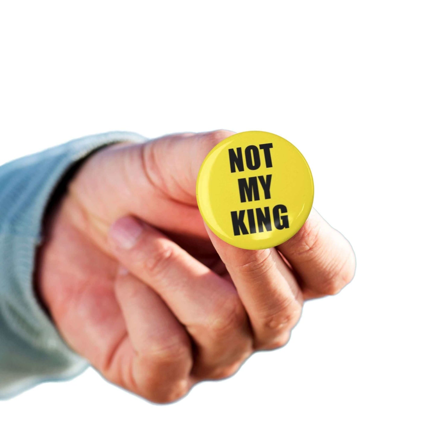 Hand holding yellow 'Not My King' anti-monarchy political pin badge, perfect for political events or everyday wear.