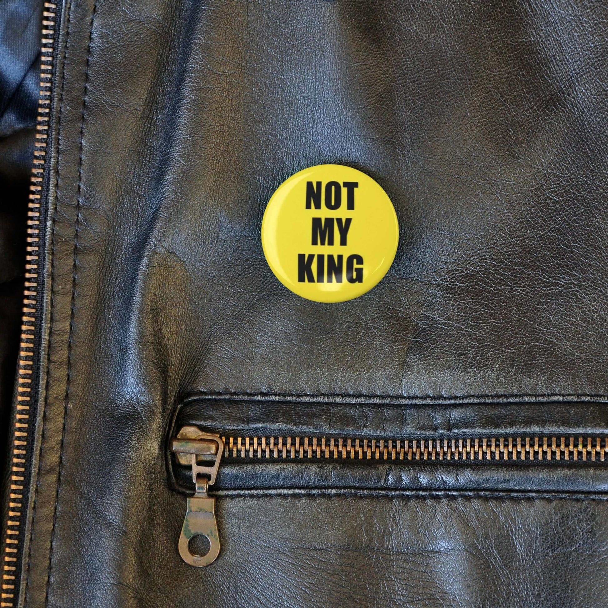 Yellow 'Not My King' anti-monarchy pin badge on leather jacket, political statement accessory.