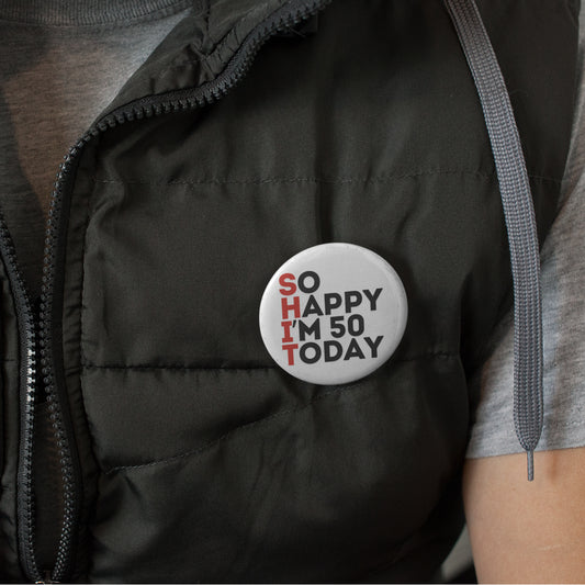An individual in a grey shirt wearing a 50th birthday badge that reads 'SO HAPPY I'M 50 TODAY', showcasing a casual style.