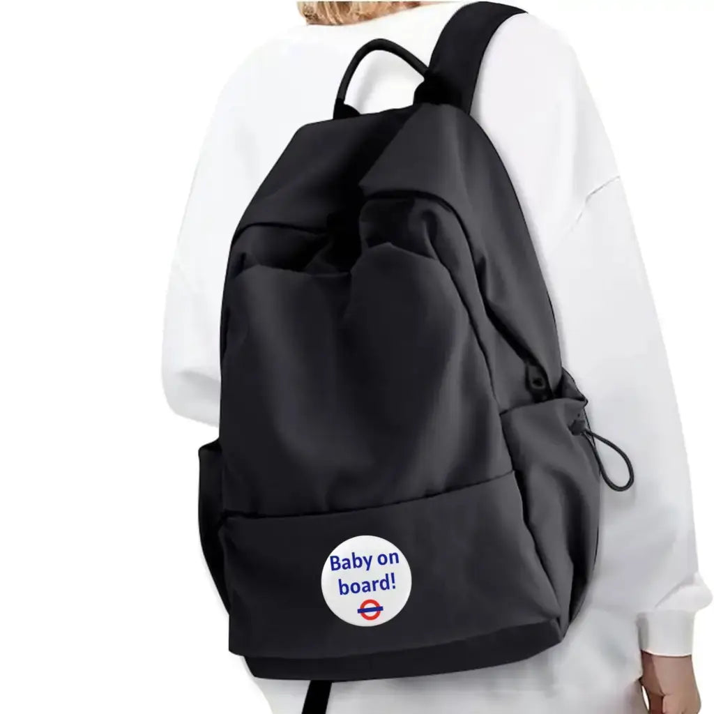 A black backpack featuring the EMU Works Baby On Board Pin, making a playful statement about the wearer’s pregnancy journey.