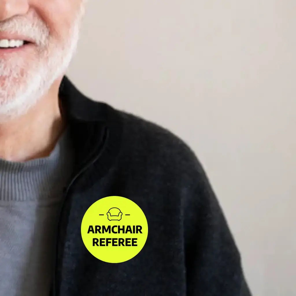 Older man wearing a Funny Football Badge that says 'Armchair Referee', emphasising a light-hearted take on football fandom.
