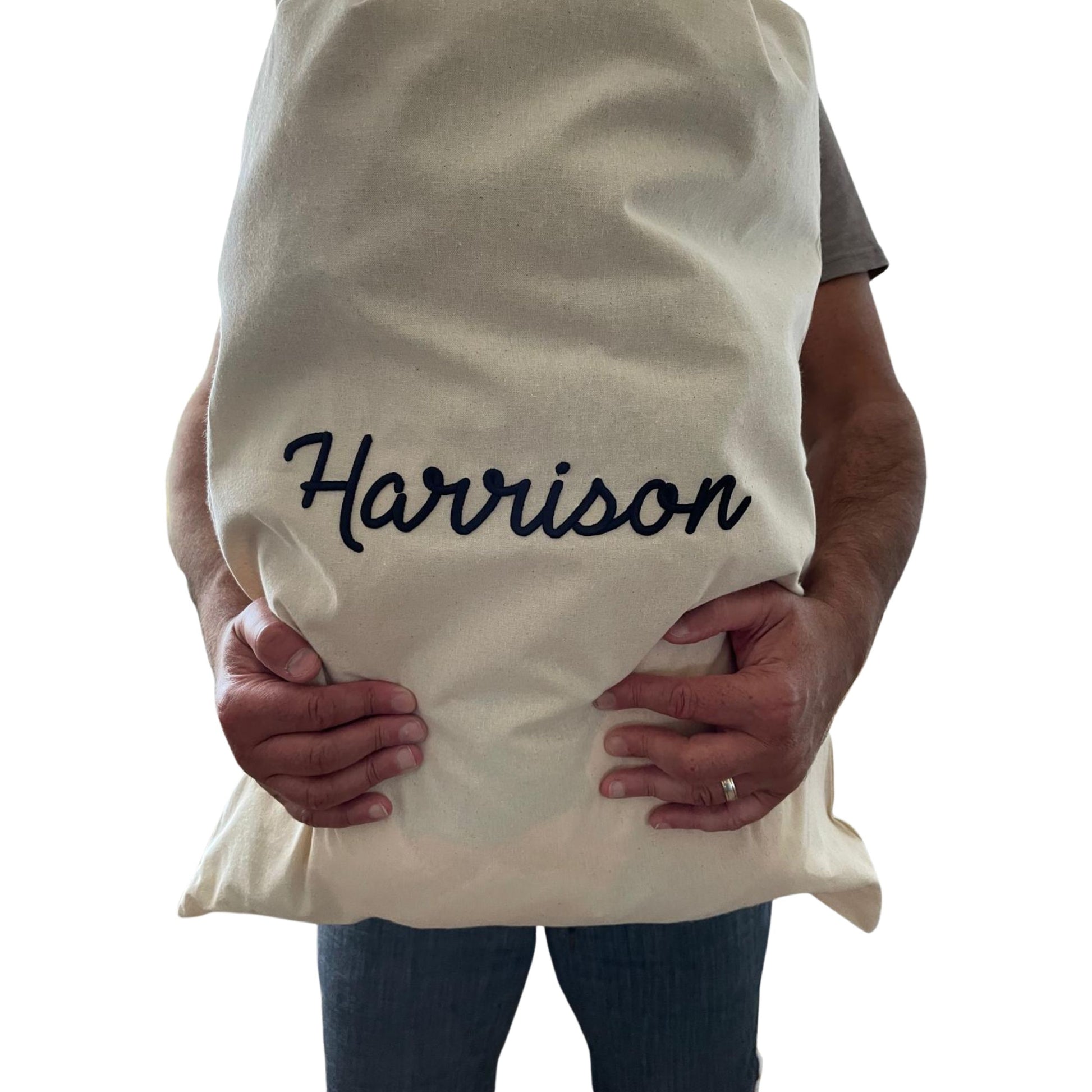 Person holding a white pillow with 'Harrison' embroidered on it against a white background