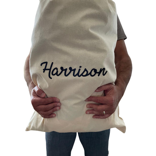 Person holding a white pillow with 'Harrison' embroidered on it against a white background