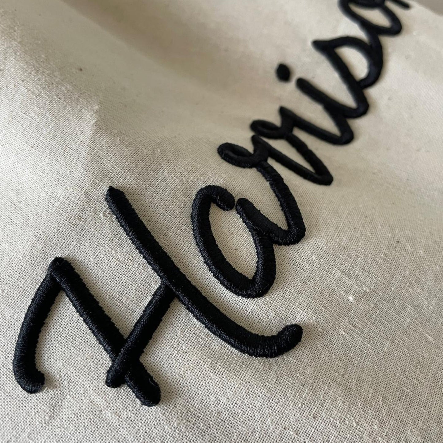 Text 'Harrison' embroidered in black on a beige fabric background