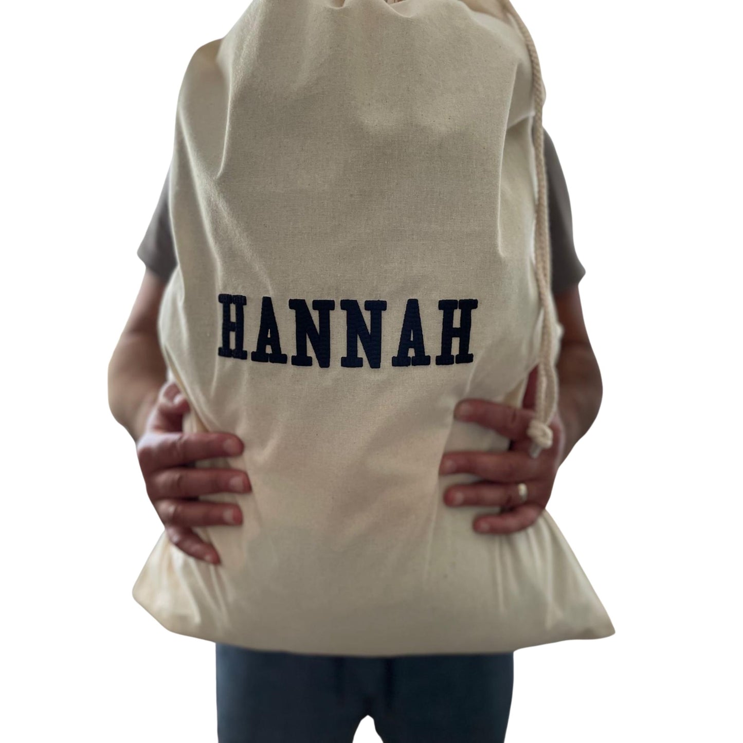 Person holding a beige drawstring bag with 'HANNAH' printed on it against a white background