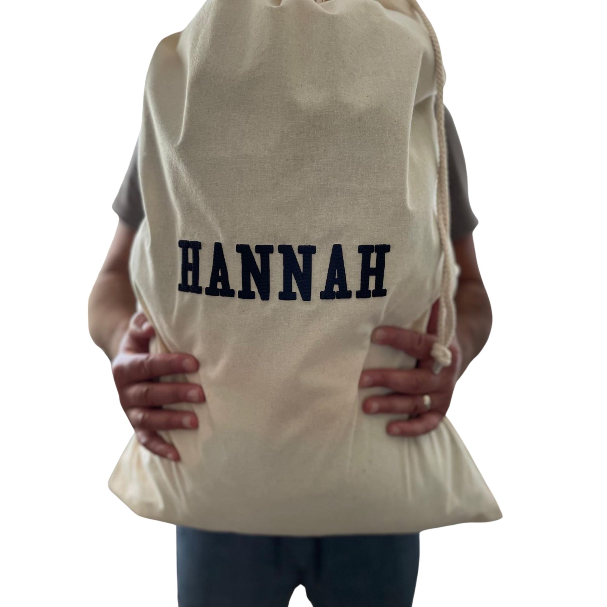 Person holding a beige drawstring bag with 'HANNAH' printed on it against a white background