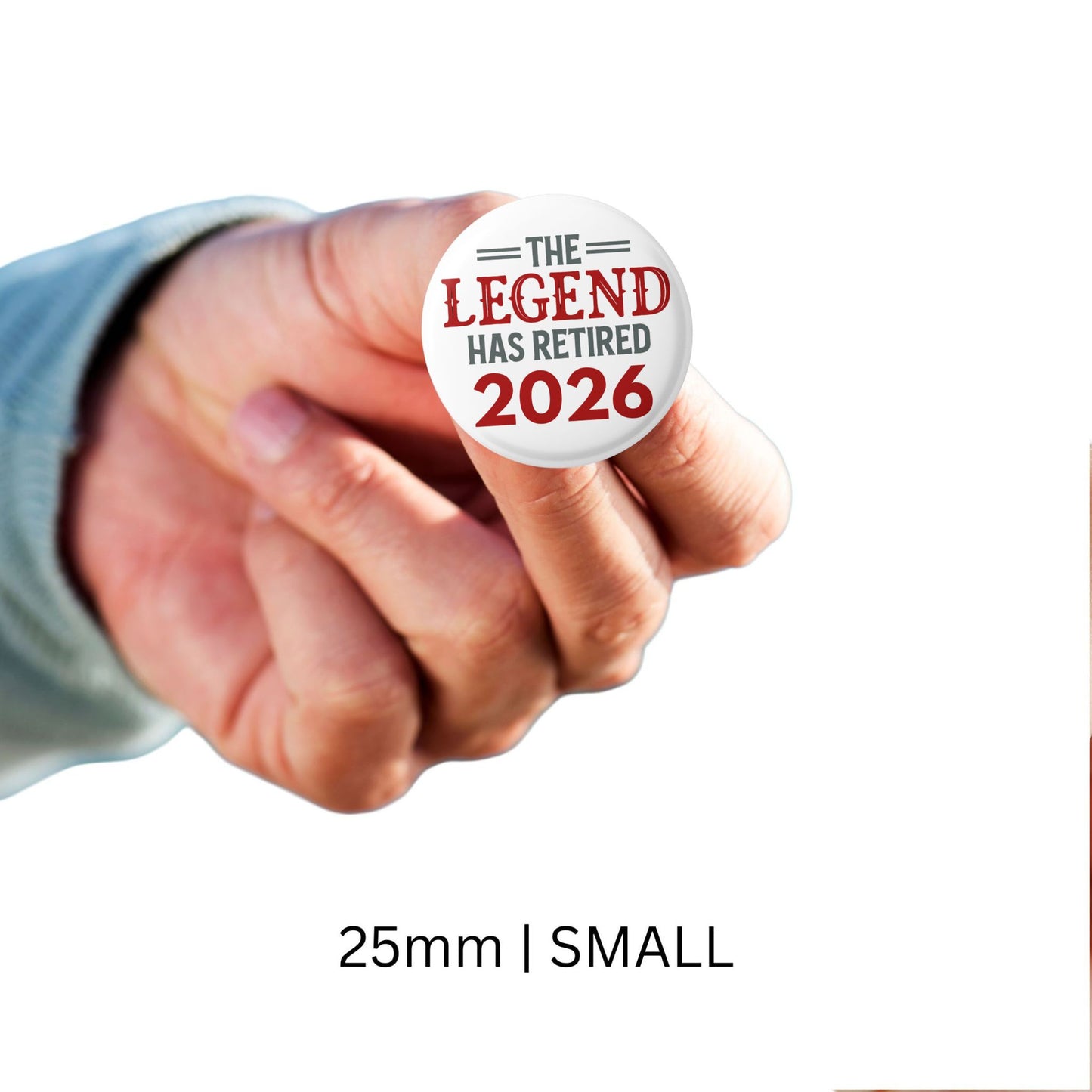 Hand holding a button with 'The Legend Has Retired 2026' text on a white background