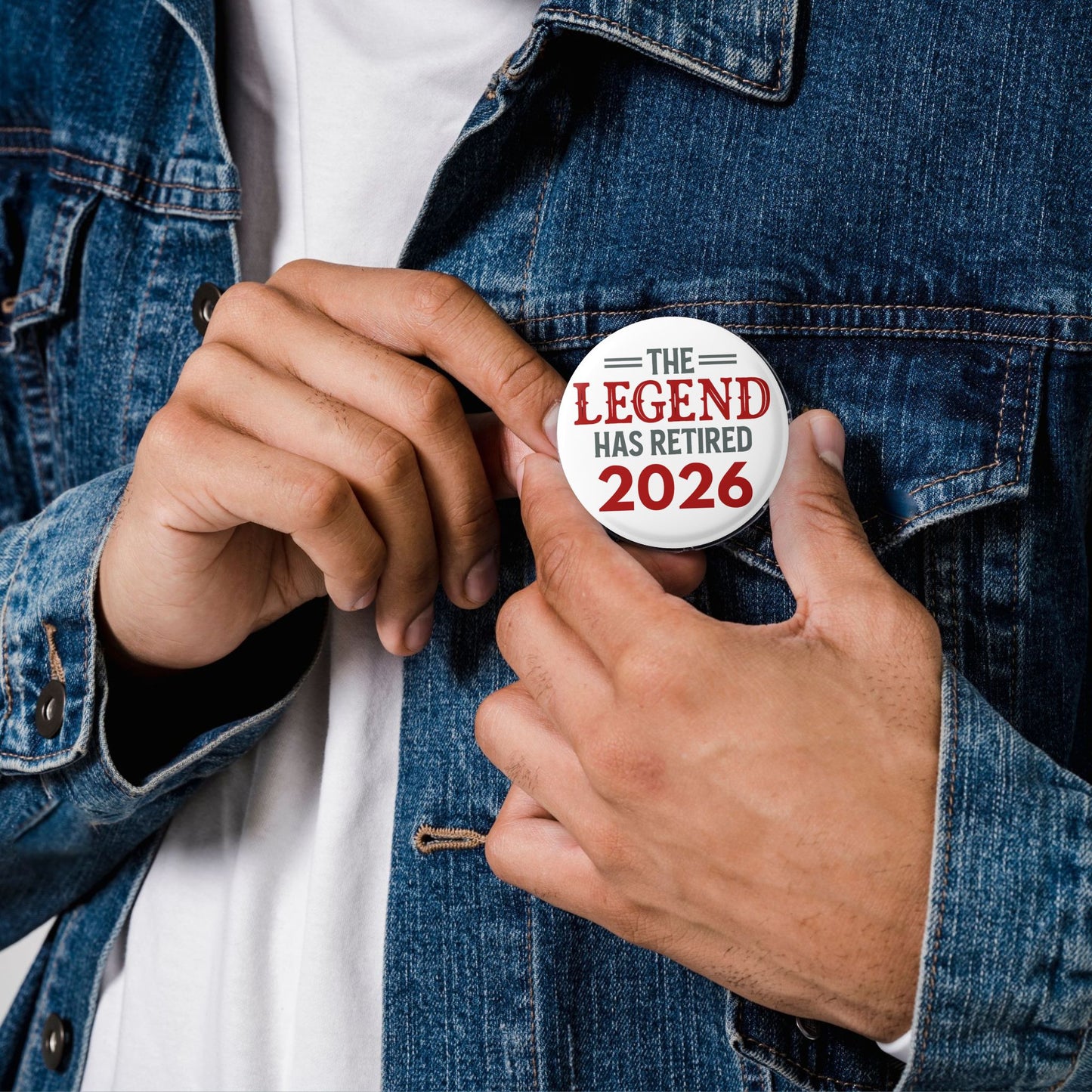 Person wearing a denim jacket and buttoning a 'The Legend Has Retired 2026' button.