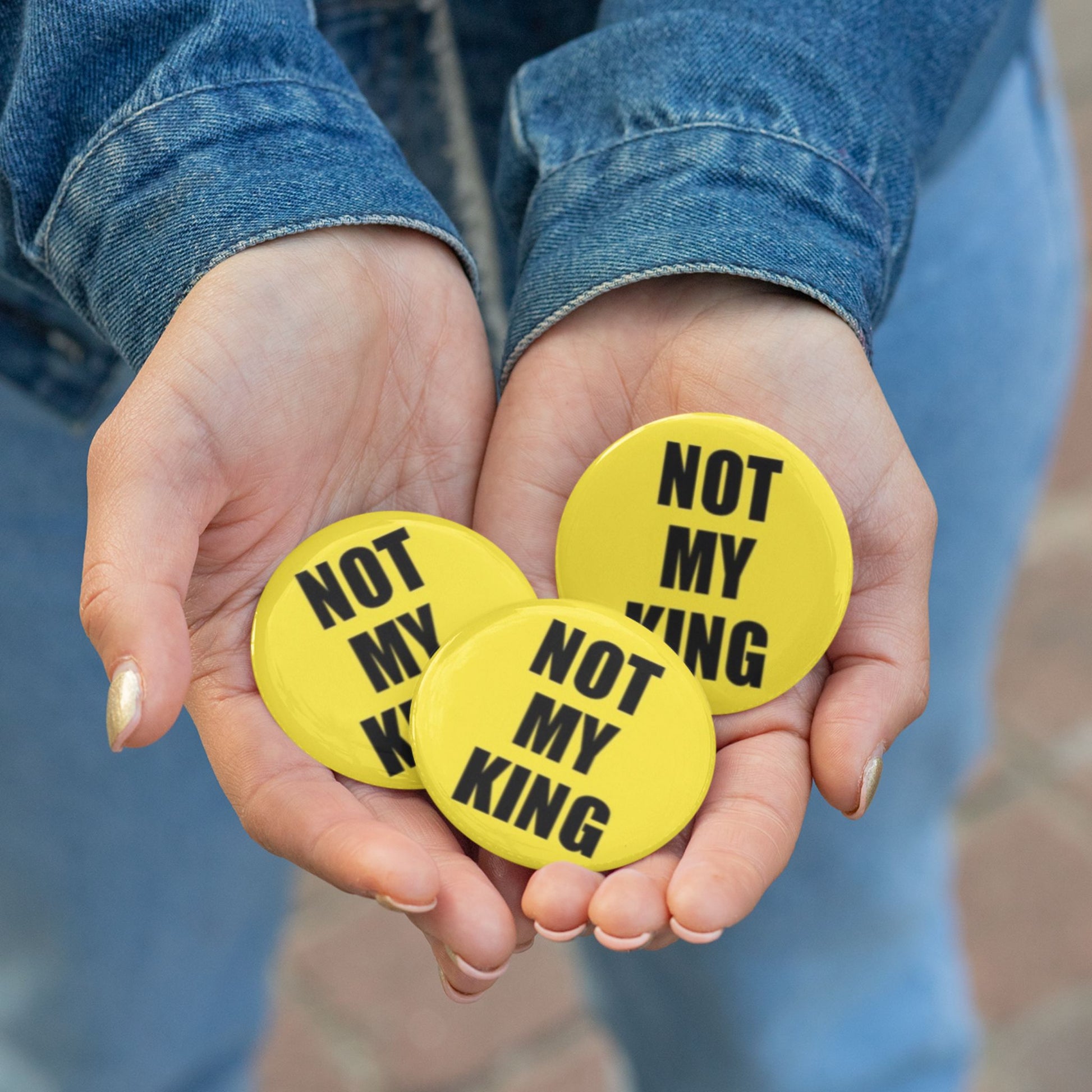 Hands holding three yellow buttons with 'Not My King' text against a blurred background.