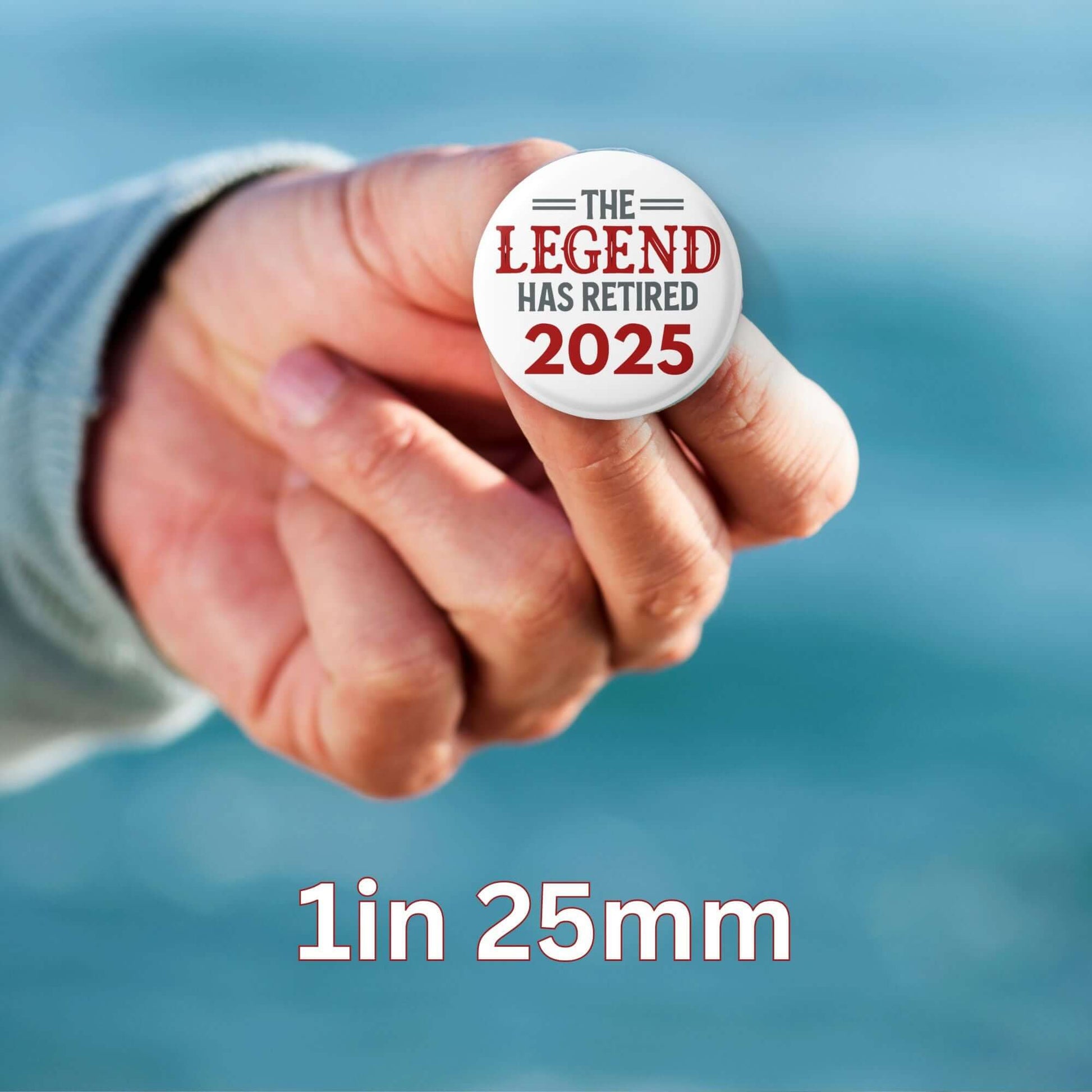 Hand holding EMUWORKS 25mm retirement badge, 'The Legend Has Retired 2025', celebrating retirement.